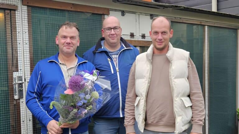 Three smiling brothers, Johan, Wim, and Herman Molendijk, standing proudly together outside their loft in Strijen while holding a massive bouquet of celebratory flowers presented by the board of Afdeling ZuidWest after their historic first and second place victory against 20634 racing pigeons from Toury.