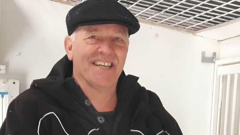A smiling Harold van de Kruijk standing proudly in front of his pigeon lofts in Monster, celebrating his legendary 1st National Pau 2026 victory with one of his elite De Kruijk Pigeons.