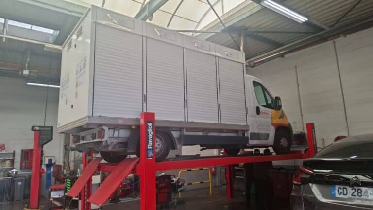 The specialized white pigeon transport truck of OLR Lasterie Zwiep raised high on a red hydraulic vehicle lift inside a mechanic workshop garage for repairs following its unexpected breakdown near Troyes in France