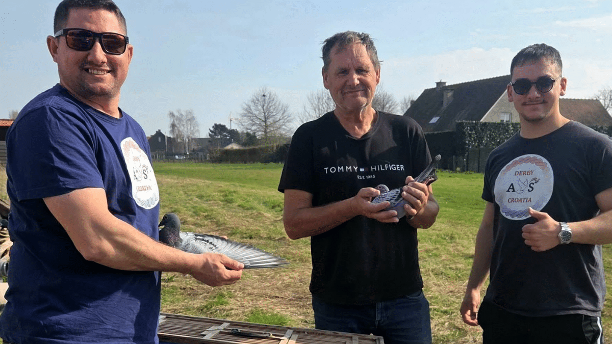 Three pigeon fanciers outdoors, two holding racing pigeons, alongside Derby As Croatia team members wearing branded shirts