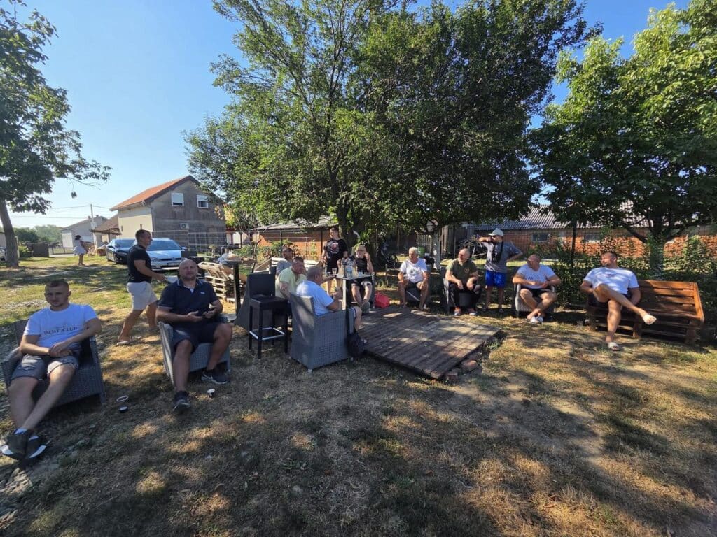Pigeon racing fanciers and guests gathered under trees enjoying Croatian hospitality during Derby AS Croatia 2026 Hotspot 1 in Đakovo