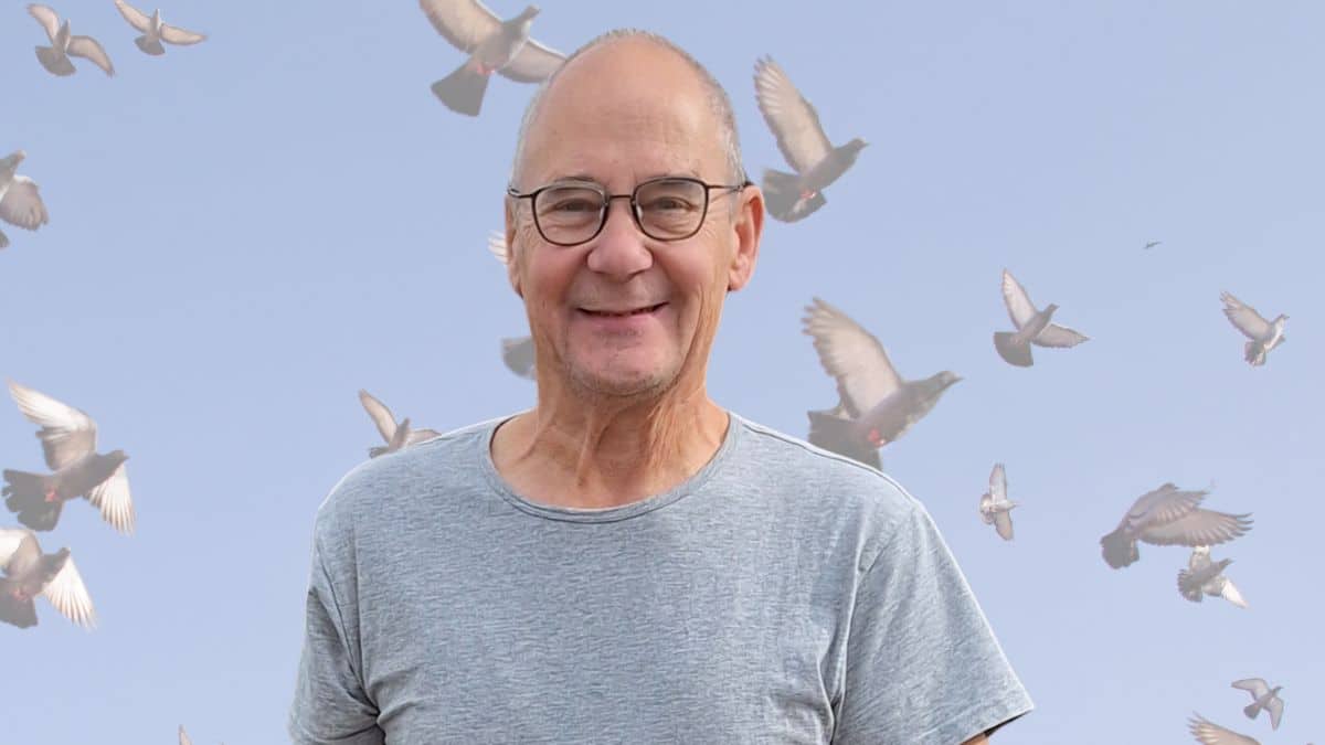 Piet Lindelauf smiling in front of a blue sky with flying Lindelauf Pigeons racing home to Vijlen