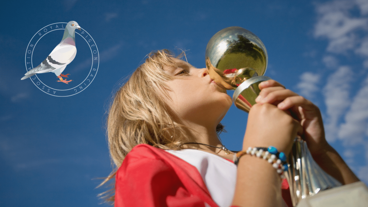 Young fancier kissing a trophy beside the Royal Pigeon Racing Association logo, celebrating the RPRA National Awards 2026.