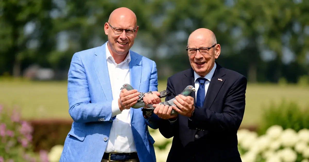 Home 6 Team Eijerkamp, Two men stand outdoors holding racing pigeons, one in a light blue blazer and the other in a dark suit.