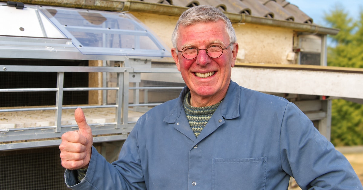 Home 2 Smiling pigeon fancier Willem de Bruijn Auction in blue workwear giving a thumbs up beside loft compartments, without text. Credit: none required